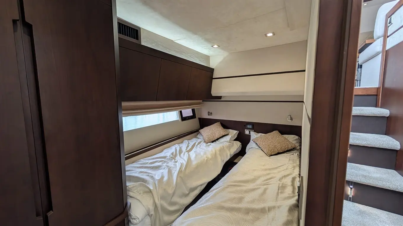 A modern boat cabin featuring two single beds with white bedding and decorative pillows, with stairs leading to an upper level.