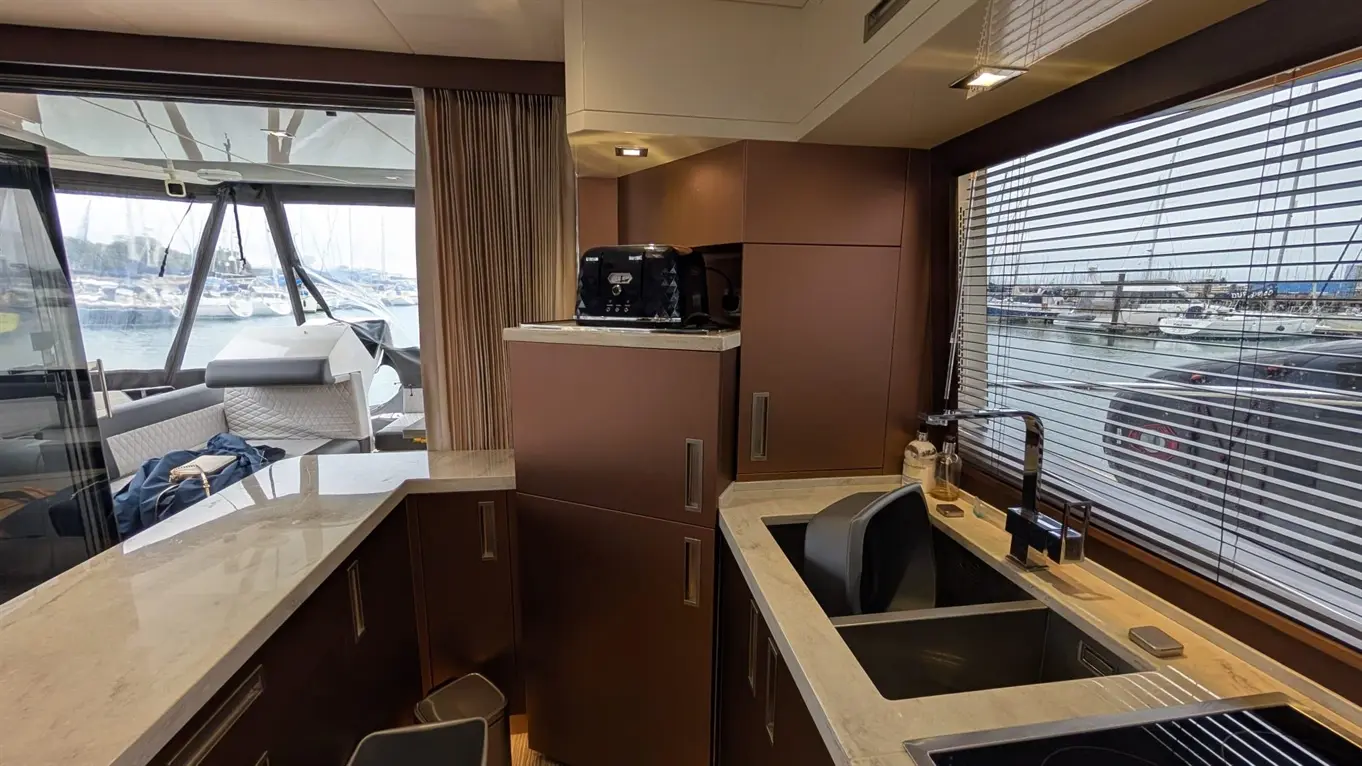 A modern boat kitchen with brown cabinetry, a sink, and a view of a marina through blinds. A toaster rests on the counter.