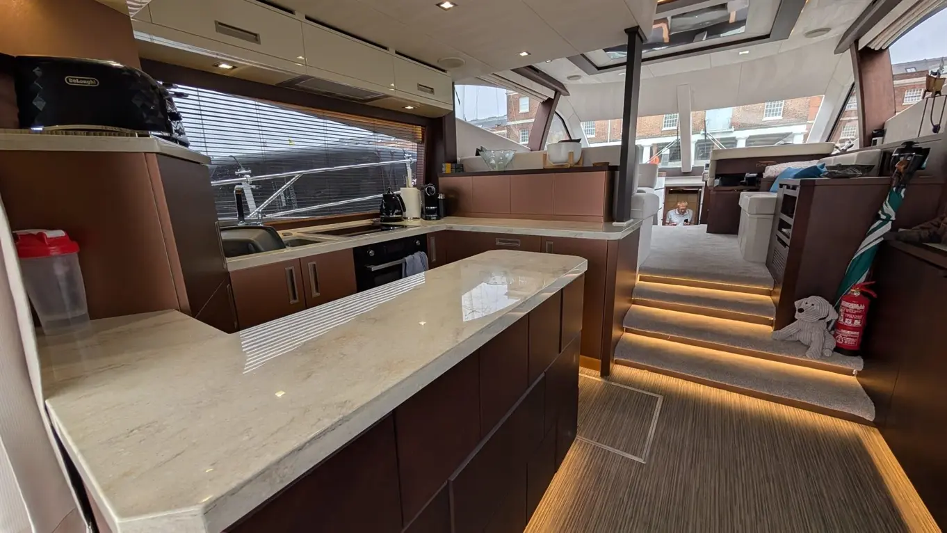 Modern kitchen on a yacht featuring a marble counter, wooden cabinets, and soft lighting, with a view of the outdoors.
