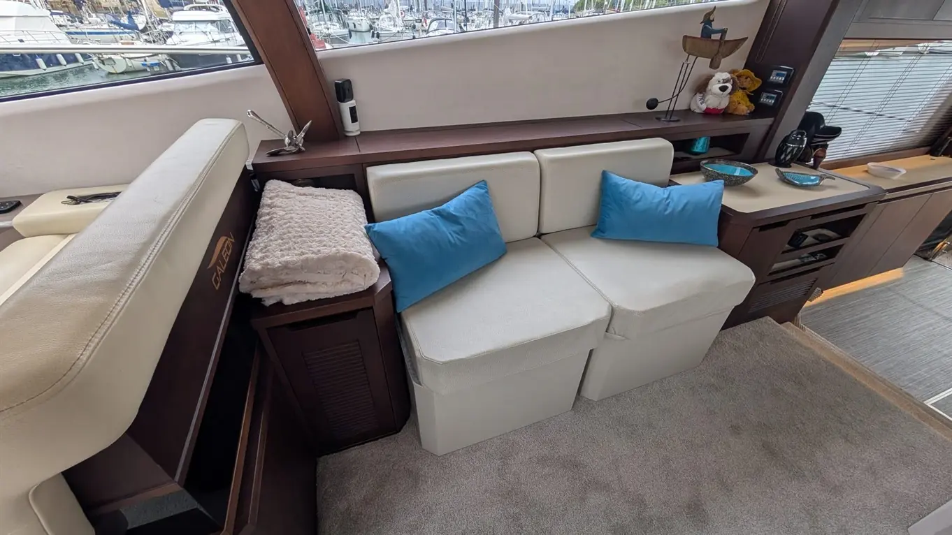 Contemporary boat interior featuring a white seating area with blue cushions, soft blanket, and views of a marina outside.