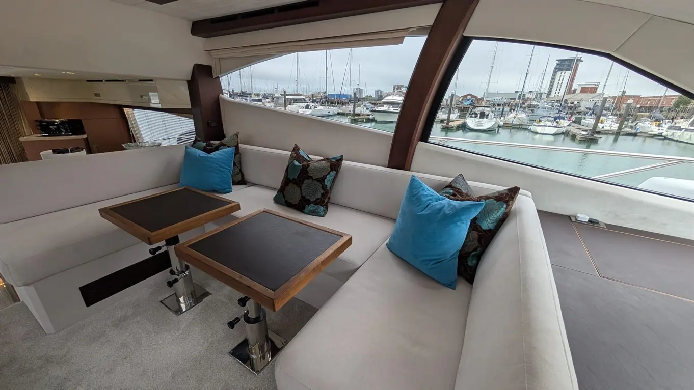 Luxurious yacht interior featuring plush seating, blue decorative cushions, and a view of the marina with moored boats.