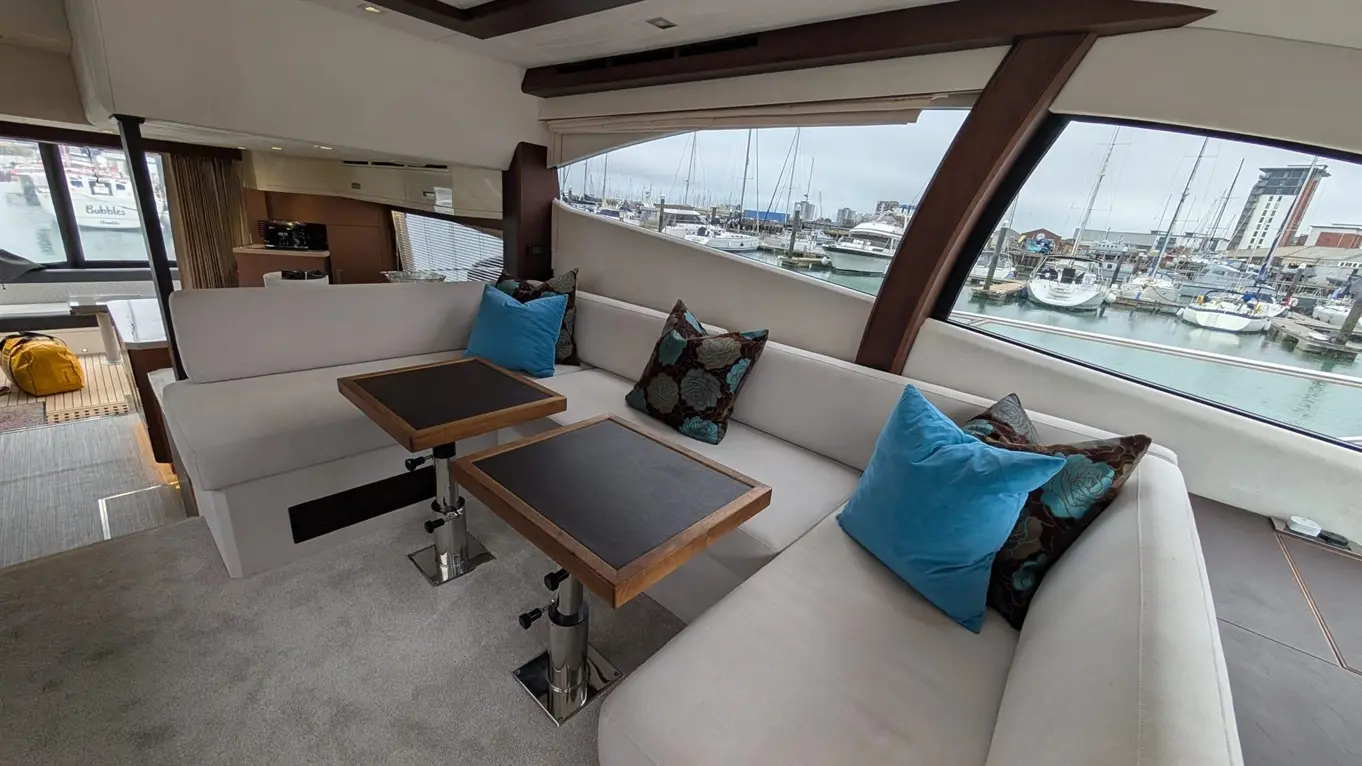 Stylish yacht interior with plush seating and marine views, features blue cushions and wooden side tables by a harbour.
