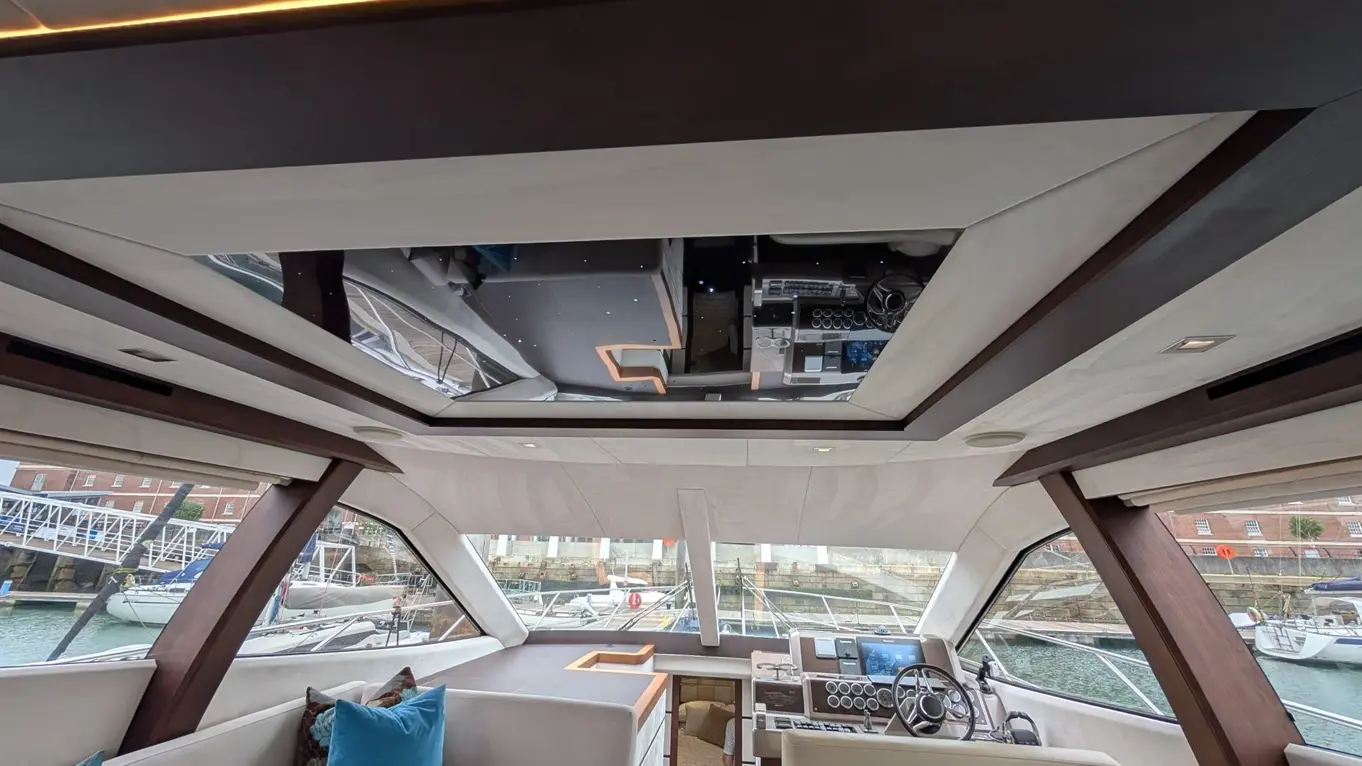 Interior of a luxury boat cabin showing sleek design, dashboard controls, large windows with a marina view, and modern furnishings.