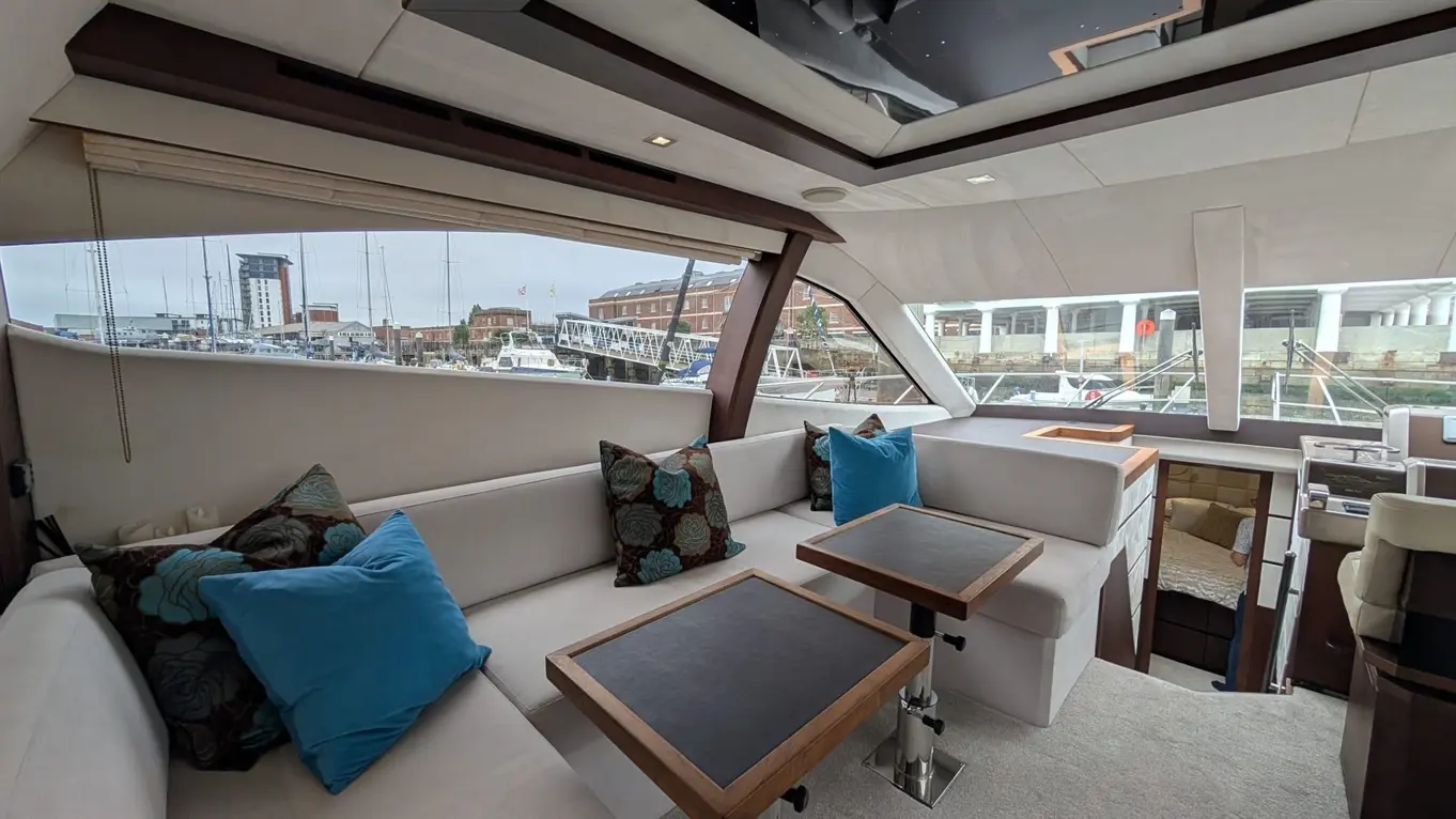 Luxury yacht interior featuring plush seating with decorative cushions, wooden tables, and a view of a marina.
