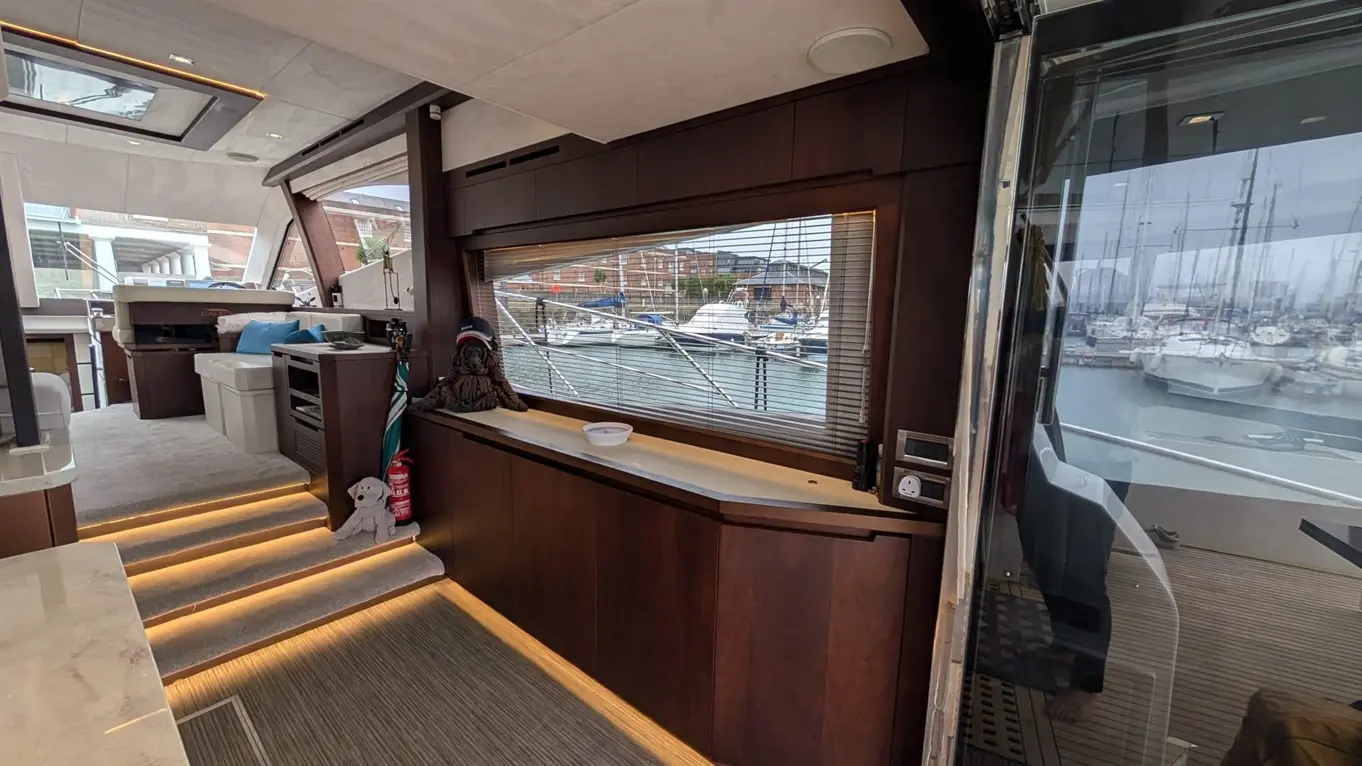 Interior of a luxury boat showing a lounge area, views of the marina, modern furnishings, and bright lighting.