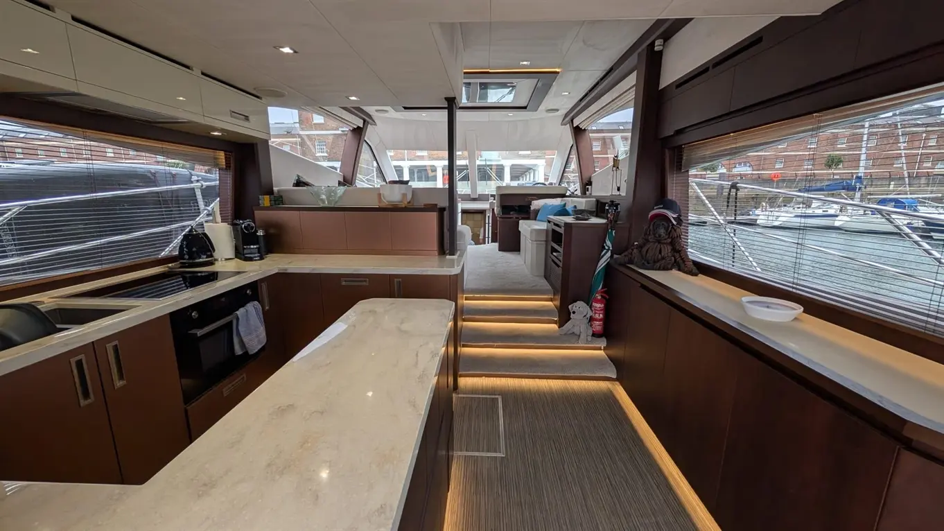 Interior of a luxurious boat featuring a modern kitchen, soft lighting, and plush seating, with views of the marina outside.