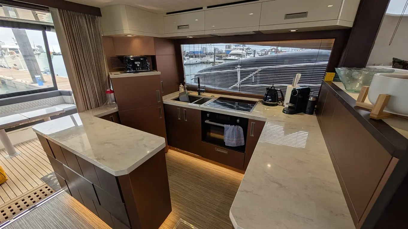 Modern yacht kitchen with marble countertops, kitchen appliances, and a view of a marina through large windows.