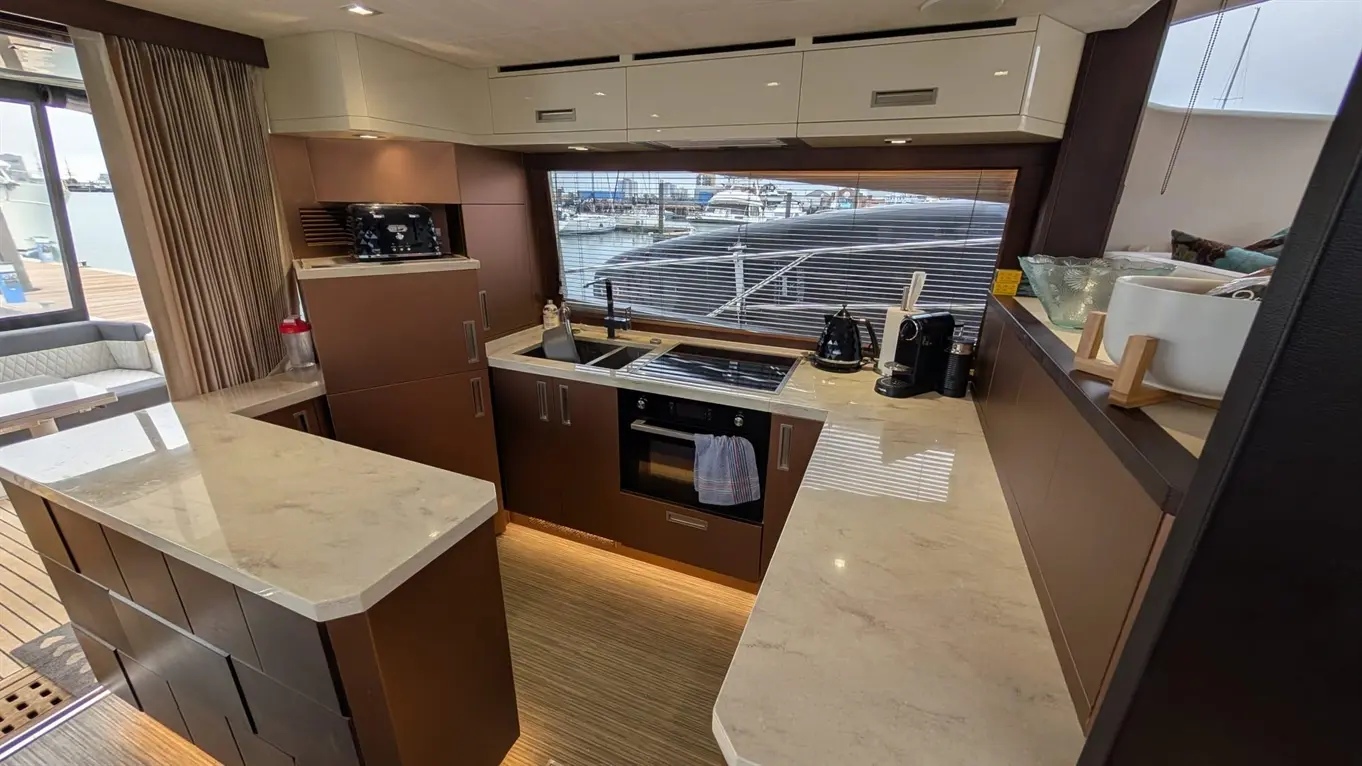 Modern yacht kitchen with sleek cabinets, marble countertops, and marine view, featuring appliances like a kettle and coffee maker.