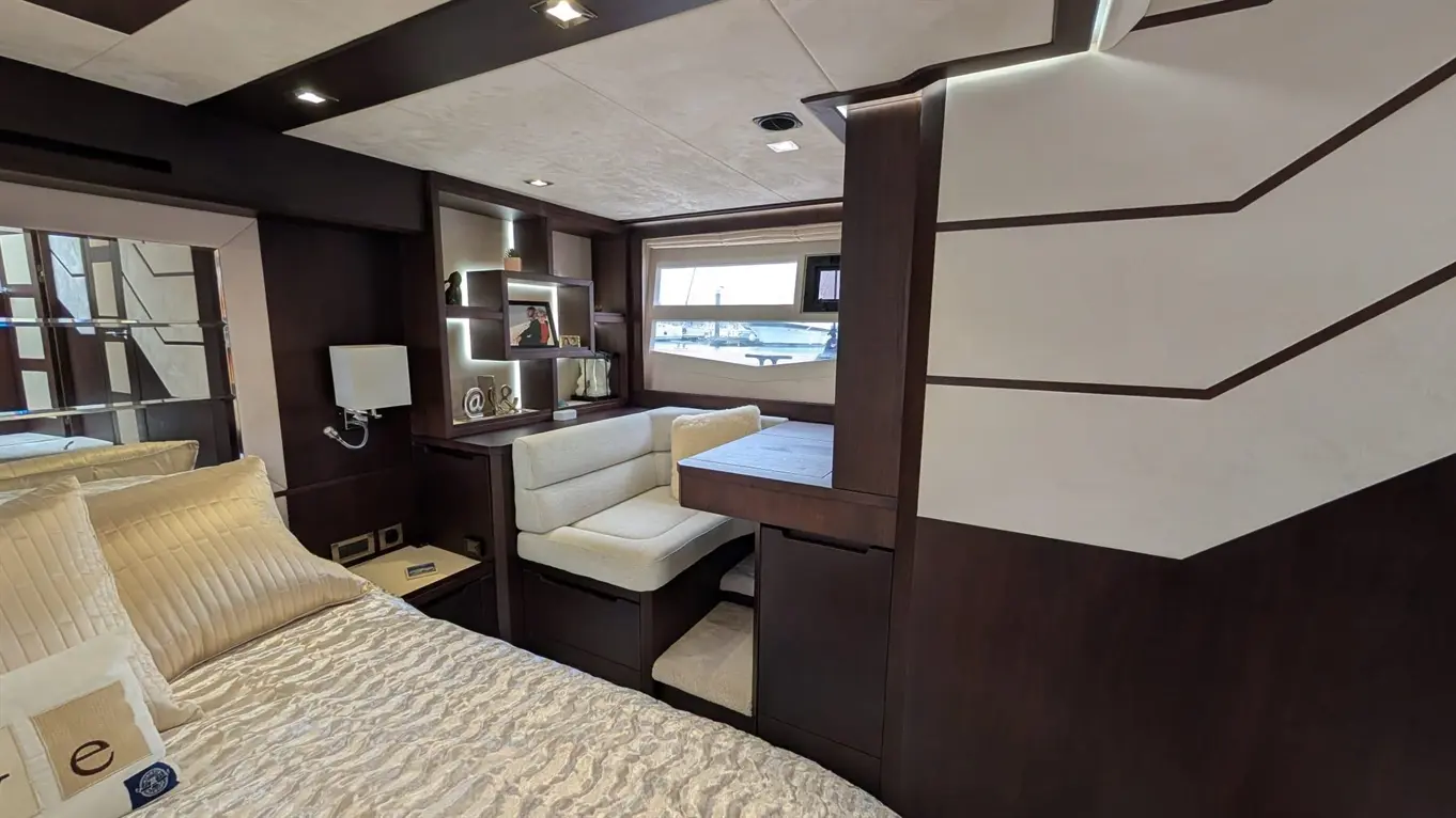 Modern interior of a luxury yacht cabin featuring a bed, seating area, and storage shelves, overlooking the water.