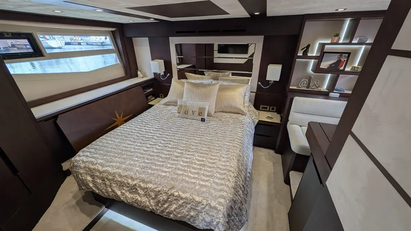 Luxurious boat bedroom featuring a double bed, decorative cushions, desk area, and windows overlooking the water. "Love" sign displayed.