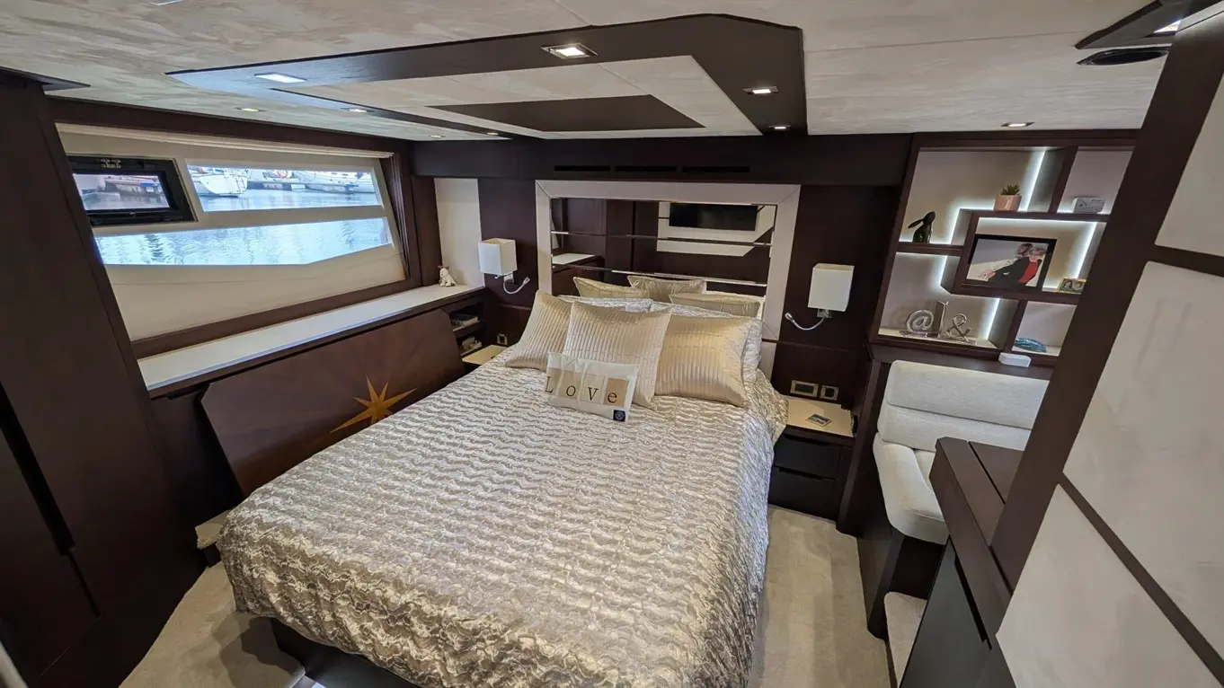 Luxury boat interior featuring a bed with golden cushions, polished wood furnishings, and scenic water views through large windows.