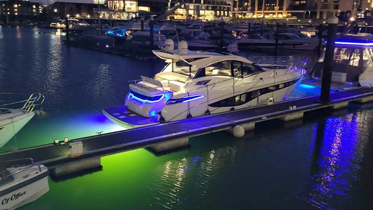 Vibrant marina scene at night featuring luxury yachts with blue lighting and reflections in the water, creating an upscale atmosphere.