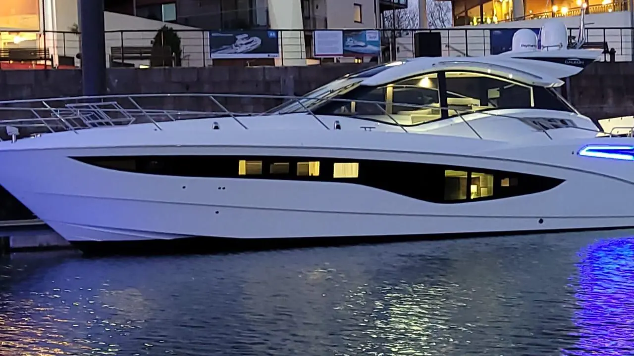 Luxury white motor yacht docked at night, illuminated by blue lights, reflecting on the water surface.