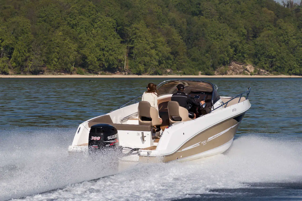 Motorboat with two people cruising on a calm lake, surrounded by greenery, with visible Suzuki 300 engine.