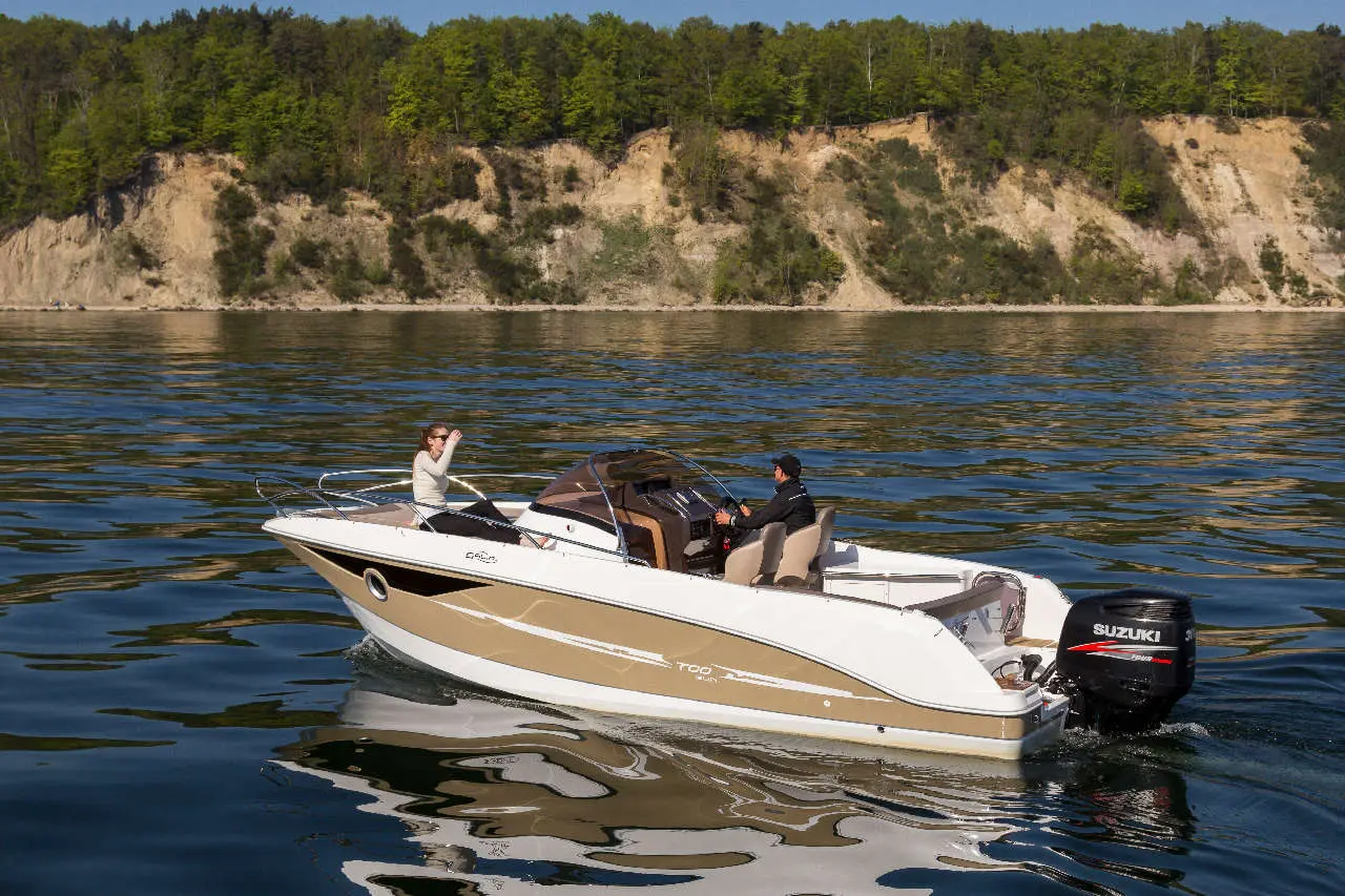 A stylish boat with two people cruising on tranquil water, surrounded by lush greenery and rocky cliffs in the background.