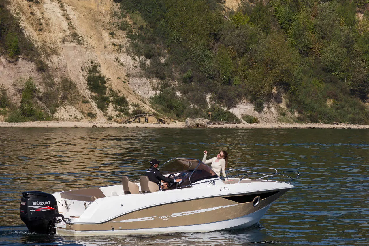 A motorboat with a Suzuki engine on calm waters, a woman joyfully gesturing while a man steers the boat.