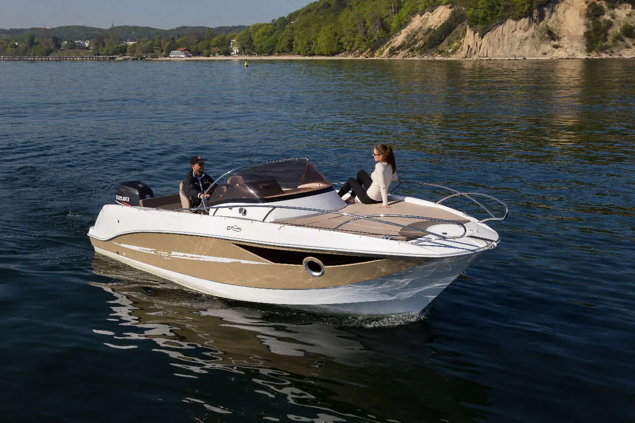 A speedboat glides through calm waters with a man steering and a woman relaxing on the bow, surrounded by greenery.
