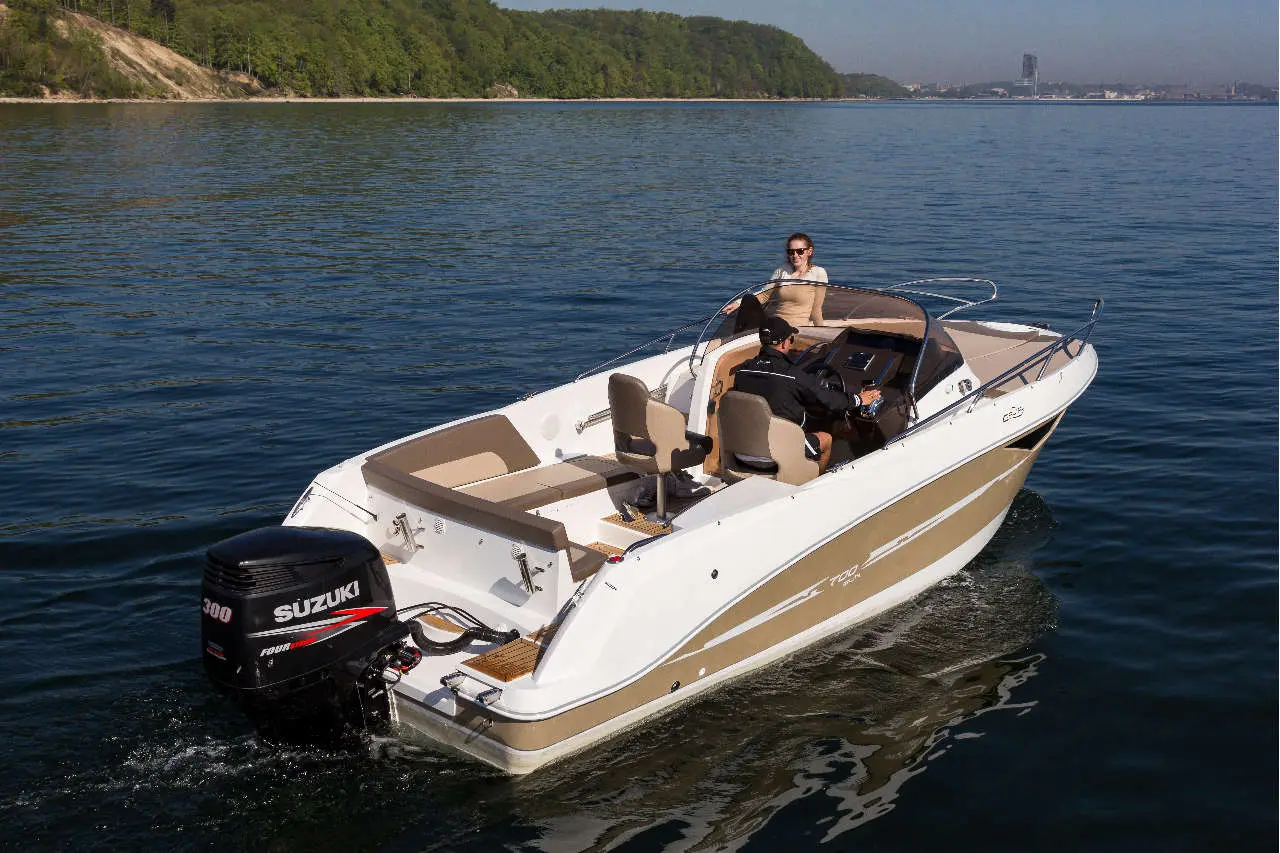 A sleek white and beige boat with two people onboard navigates calm waters, showcasing a Suzuki 300 engine.