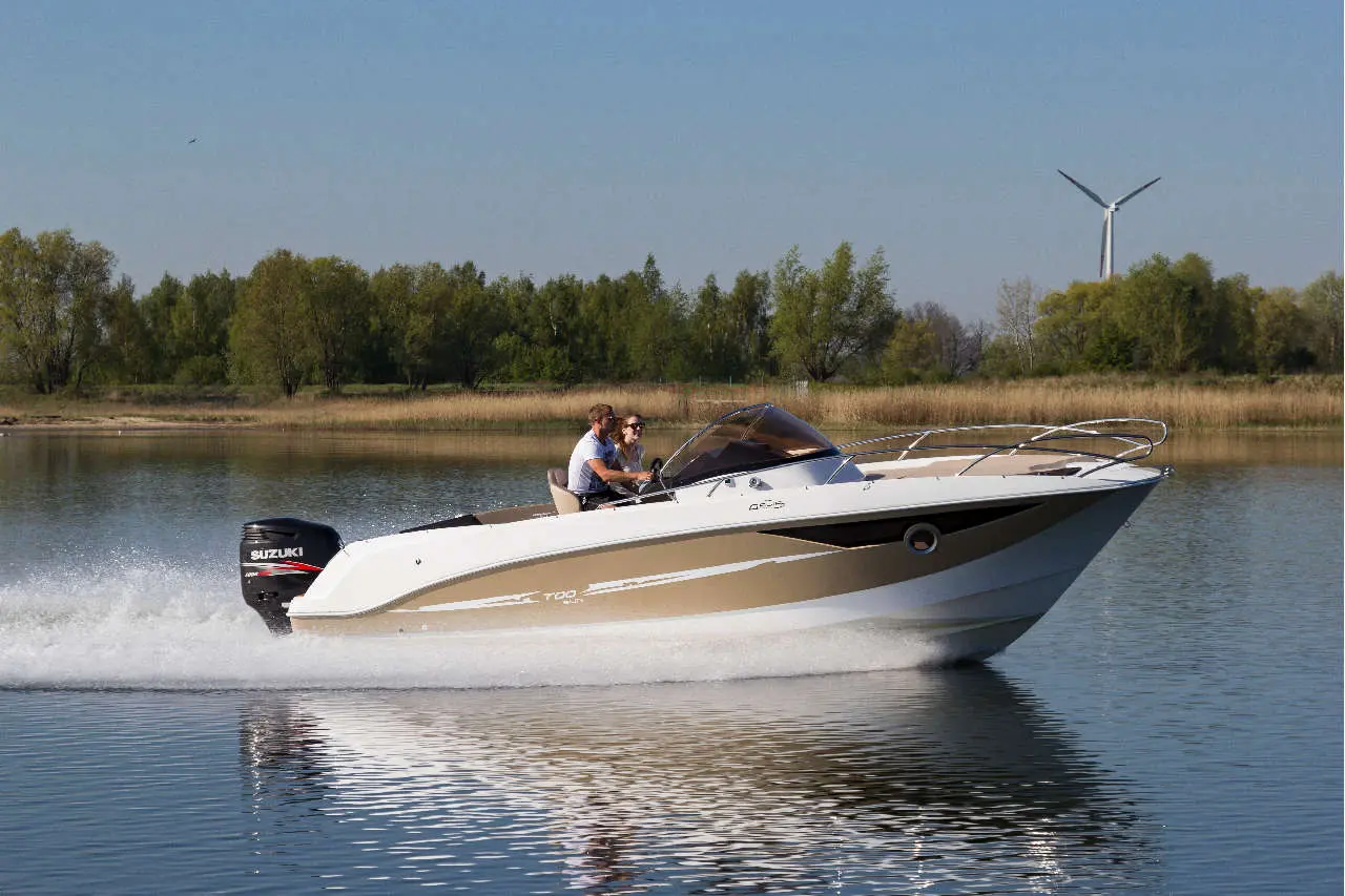 A couple enjoys a ride in a white and gold speedboat on a serene lake, with trees and a wind turbine in the background.