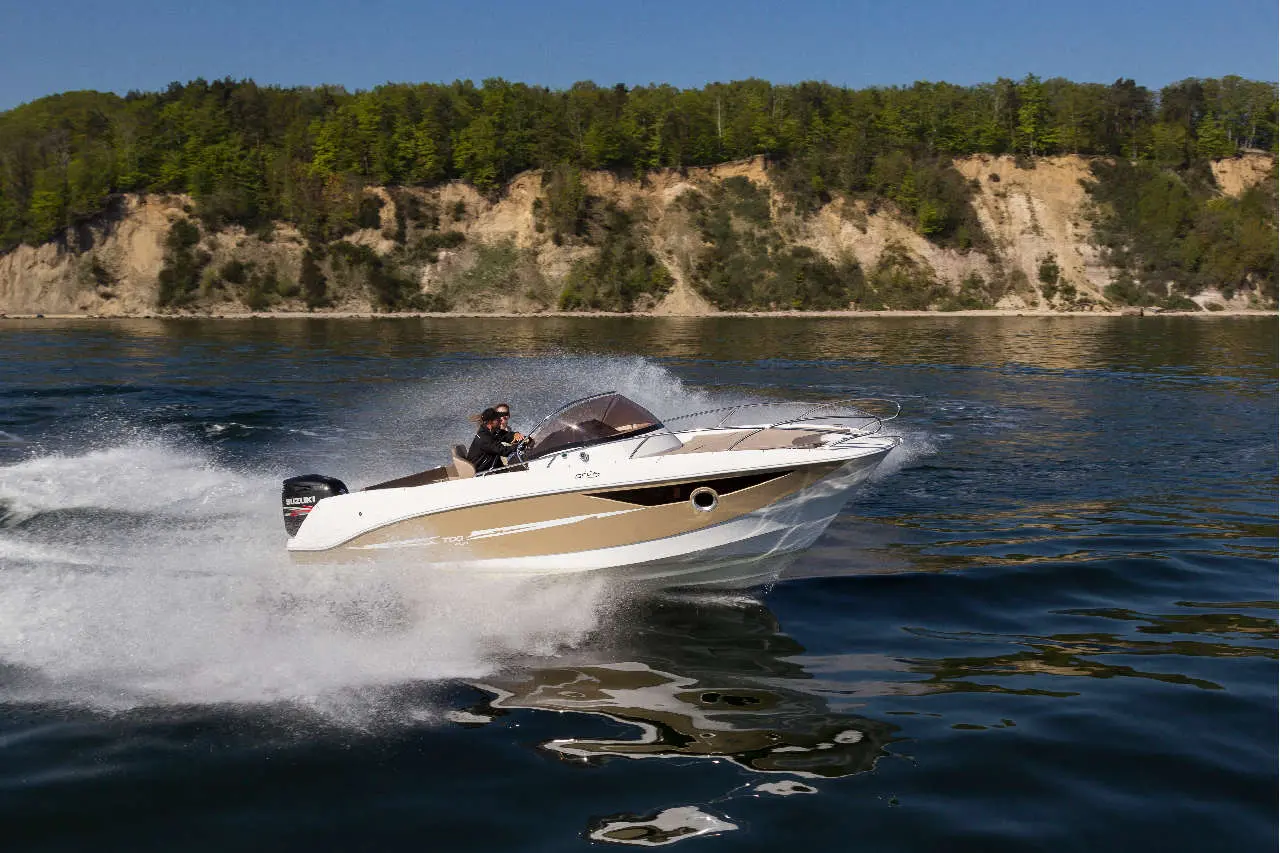 A speedboat glides across the water, creating splashes, with a driver steering confidently in a scenic landscape.