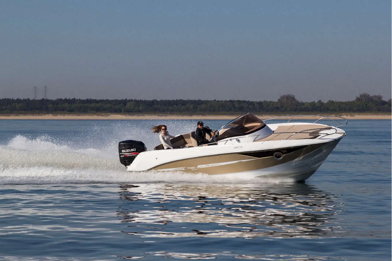 A boat with two people speeds across a calm lake, with shimmering water and a forested shoreline in the background.