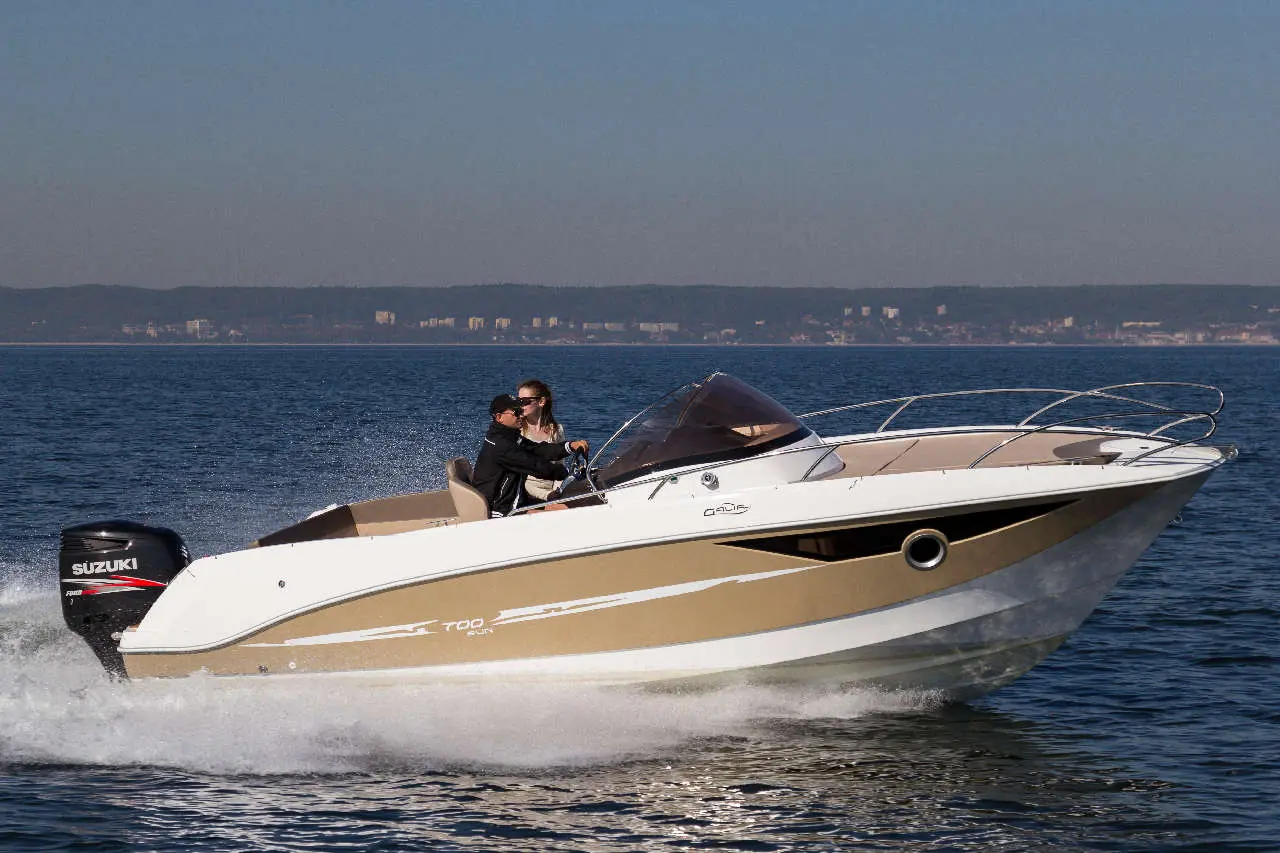 A couple enjoys a speedboat ride on calm waters, showcasing a Suzuki outboard motor, with a clear skyline in the background.