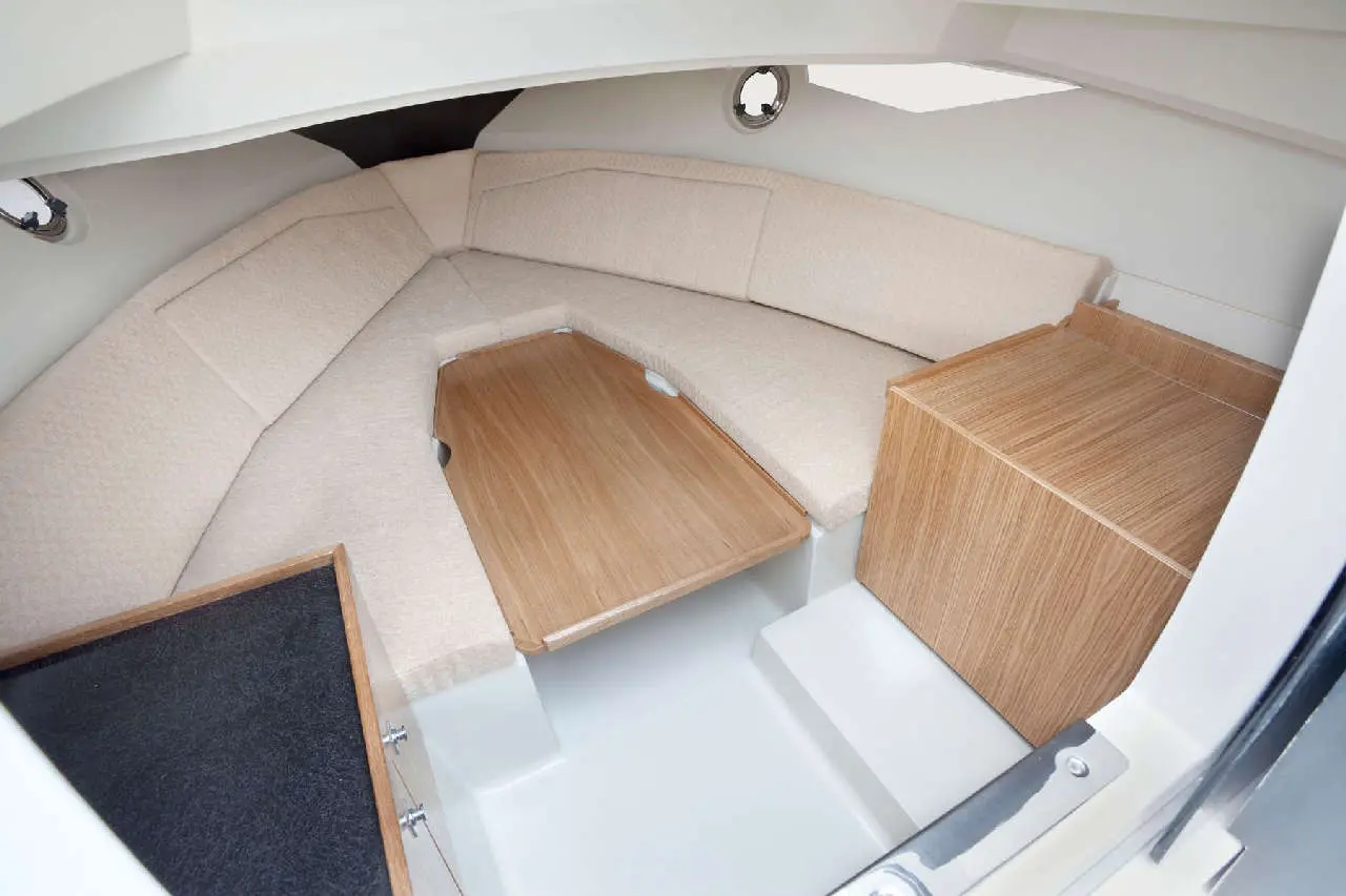 Interior of a modern boat featuring cushioned seating, a wooden table, and storage cabinets in a light, airy space.