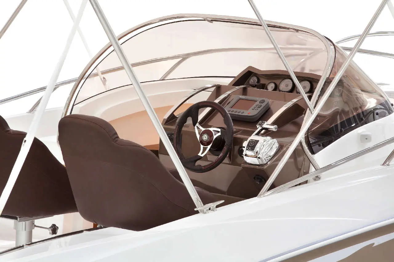 Boat cockpit interior featuring a steering wheel, control panel, two brown seats, and transparent canopy.