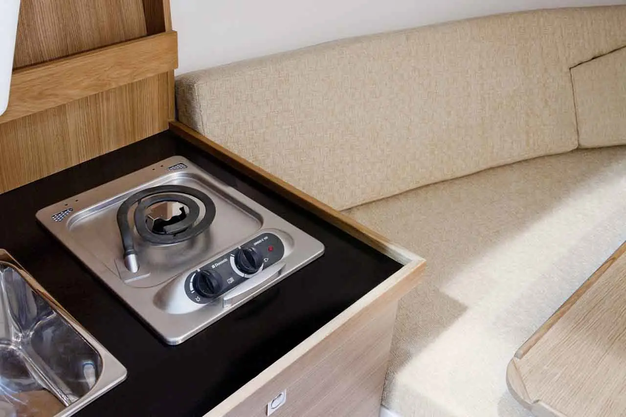 Compact kitchen area featuring a stainless-steel gas hob, dial controls, and a sink, with a beige upholstered seating arrangement.